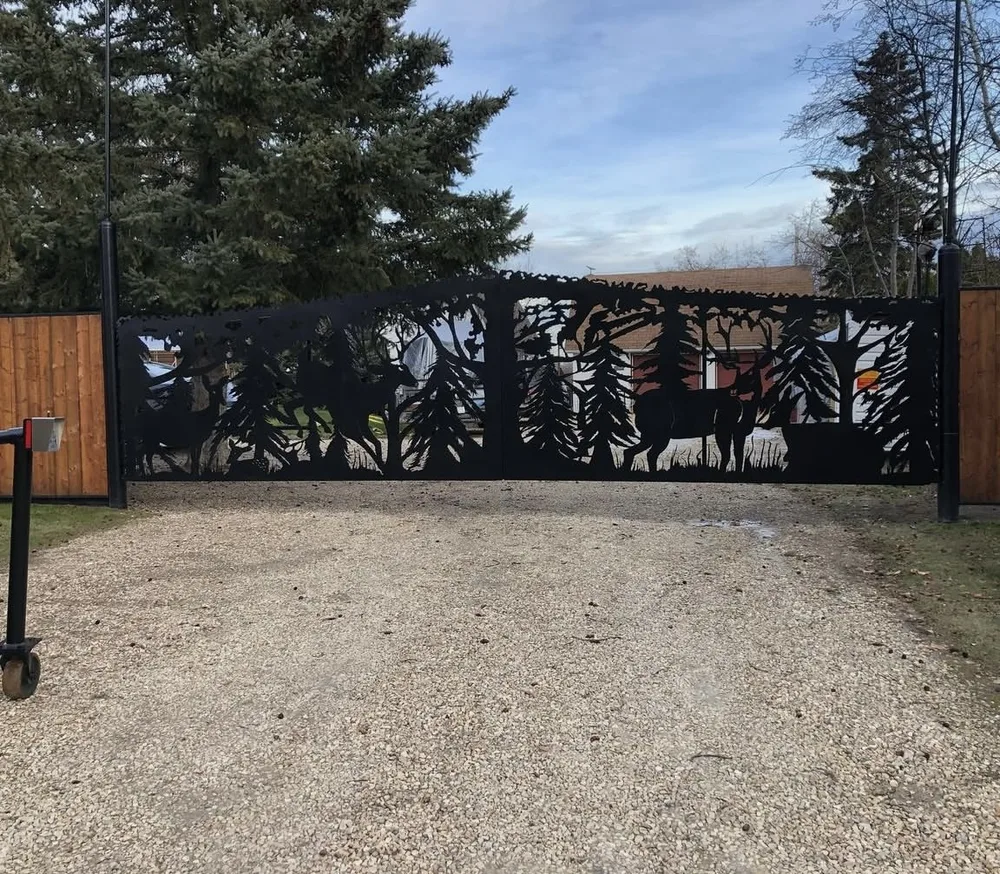 Wide black powder-coated driveway gate with wildlife and forest cutout artwork